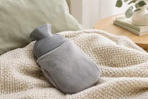 Bouillotte grise nervurée de 1,8 litre avec pochette pour la main, posée sur un plaid clair