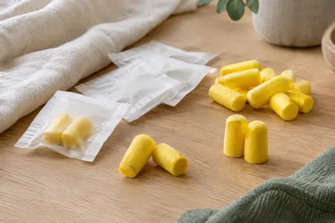 Bouchons d’oreilles classiques en mousse jaune présentés avec leurs sachets individuels sur un linge clair.