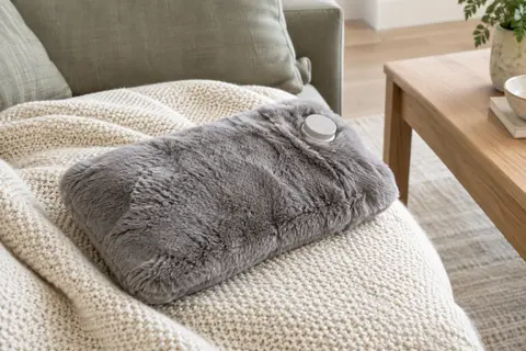 Bouillotte de 2 litres avec housse grise douce posée sur un plaid ivoire dans un intérieur serein.