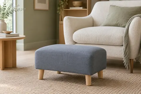 Repose-pieds rectangulaire gris bleu avec assise rembourrée et pieds en bois clair dans un salon lumineux.