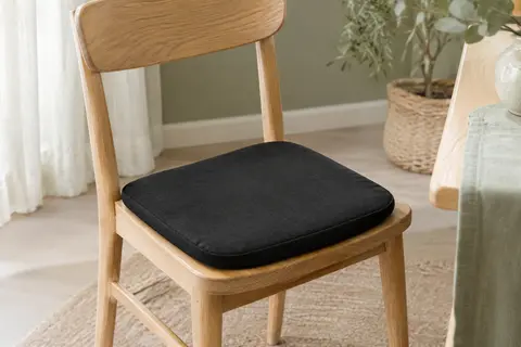 Coussin d’assise noir en mousse à mémoire de forme posé sur une chaise en bois clair dans un bureau lumineux.