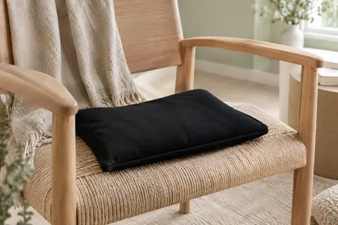 Coussin thermique noir Tampen posé sur un fauteuil clair dans un intérieur lumineux aux tons naturels.