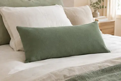 Oreiller rectangulaire vert à mémoire de forme posé sur un lit clair dans une chambre lumineuse.
