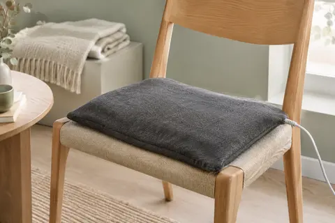 Coussin chauffant rectangulaire en flanelle gris foncé posé sur un fauteuil en bois clair